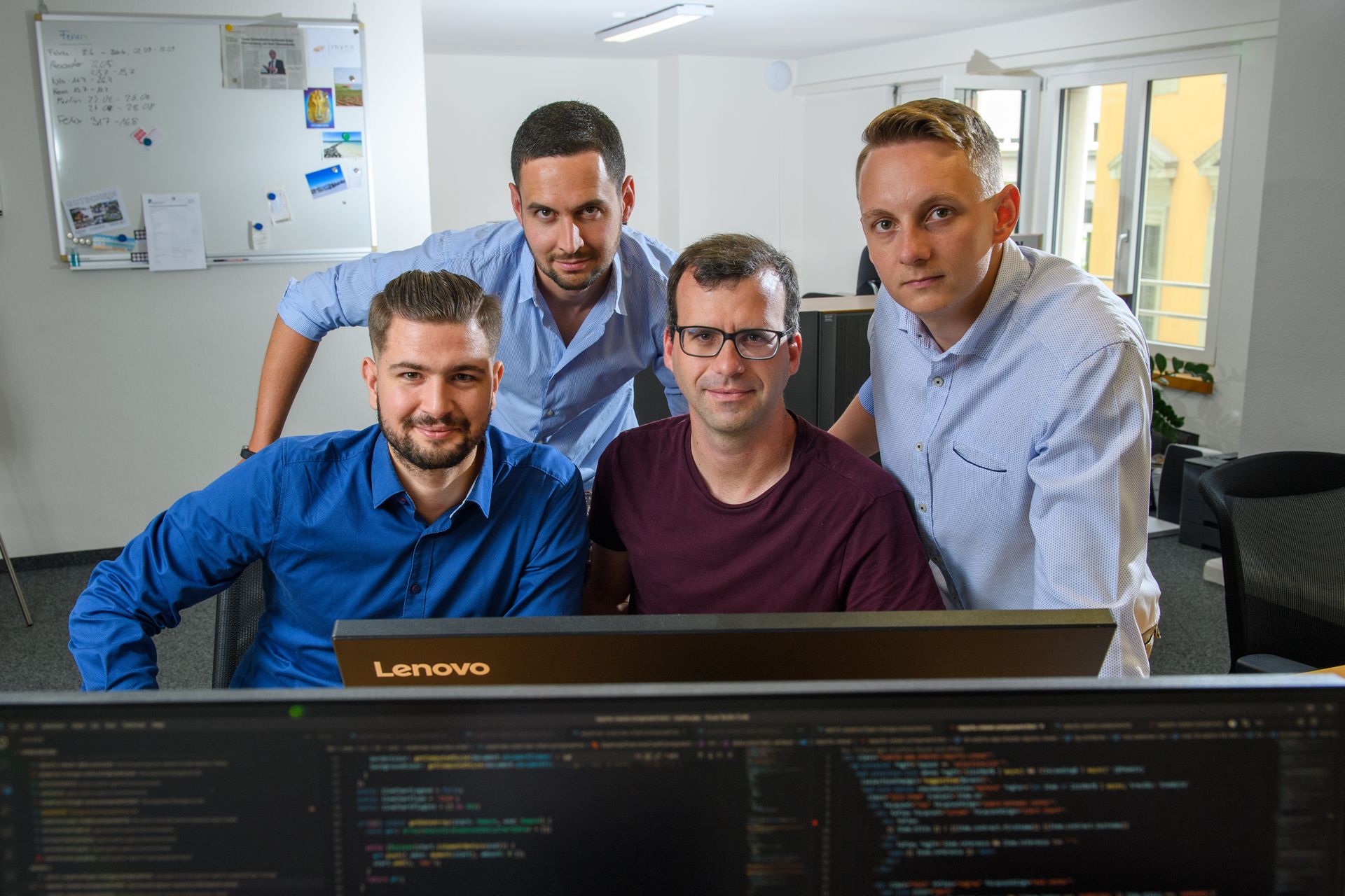 A group of men are posing for a picture in front of a computer monitor.