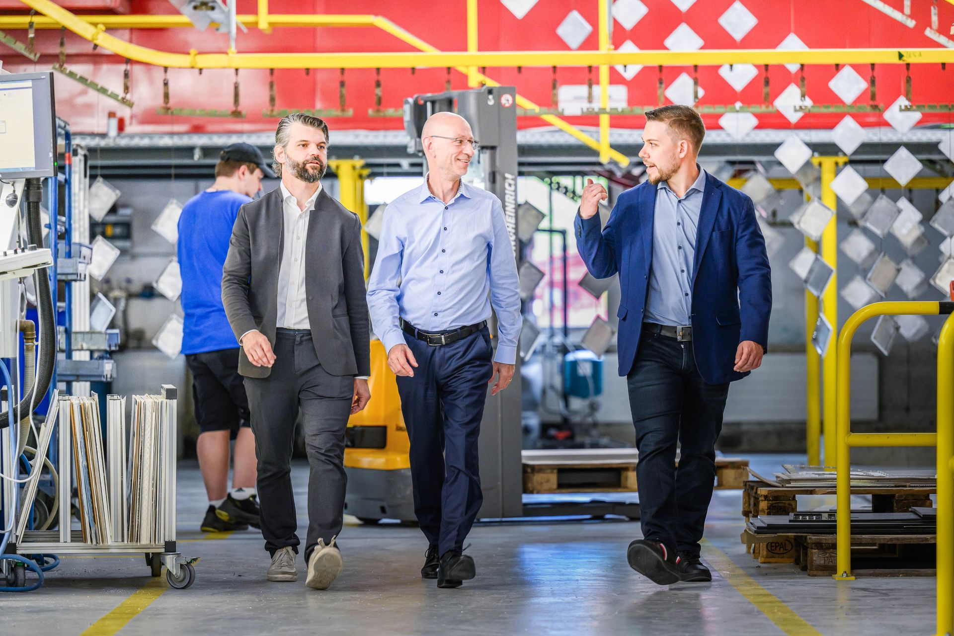 Drei Männer gehen durch eine Fabrik und unterhalten sich.