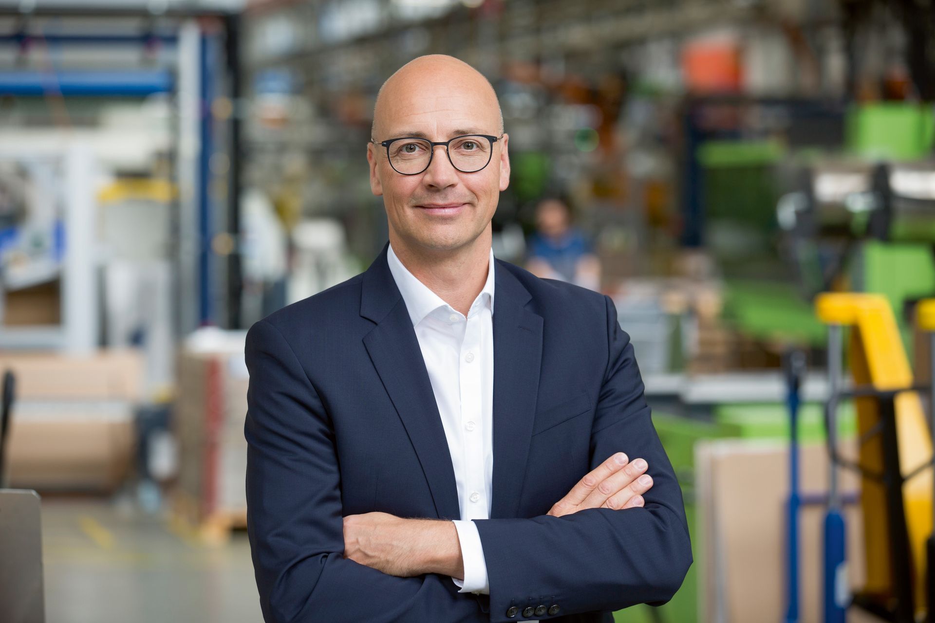 Andreas Müller, CEO Georg Fischer AG in a suit and glasses is standing in a factory with his arms crossed.