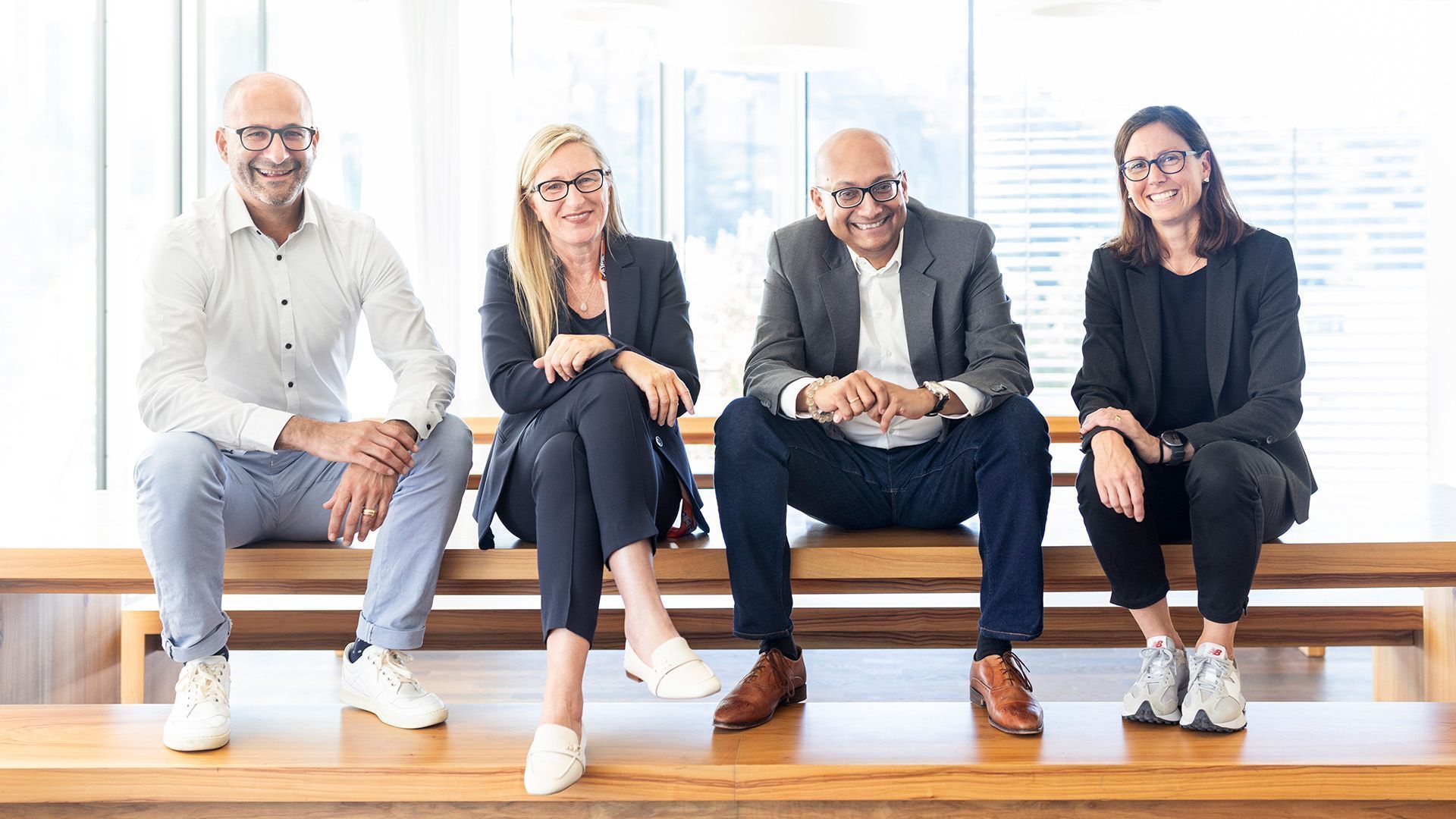 Two people of the economic promotion team and two of the Johnson Controls GmbH are sitting on a wooden bench.