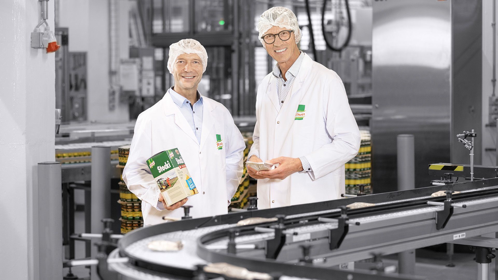 Two men in lab coats are standing next to each other in a factory.