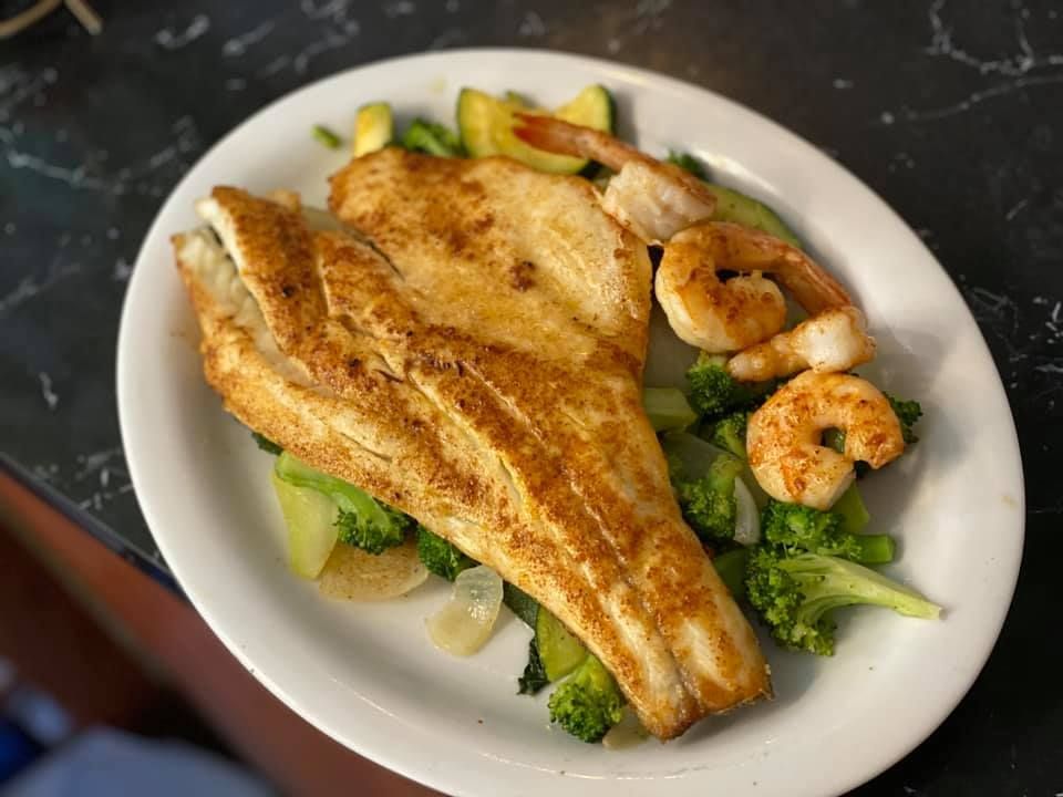 Grilled fish fillet with shrimp and broccoli on a white plate