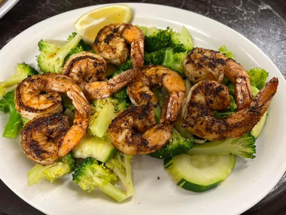 Grilled shrimp over broccoli and cucumber slices with a lemon wedge on a white plate