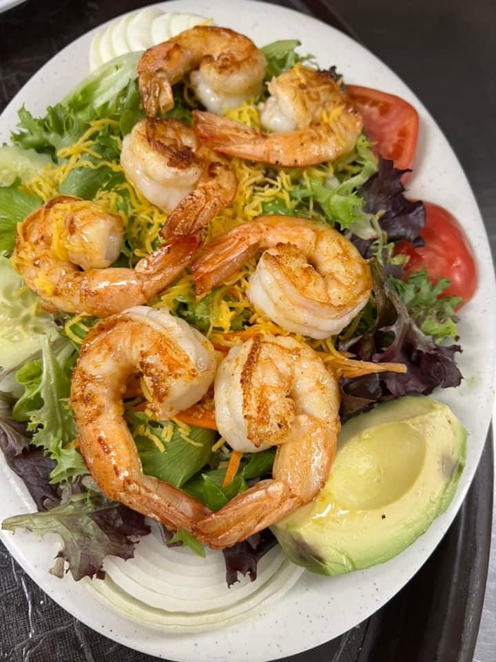 Shrimp salad with avocado, mixed greens, tomato, cucumber, and lemon wedges on a white plate