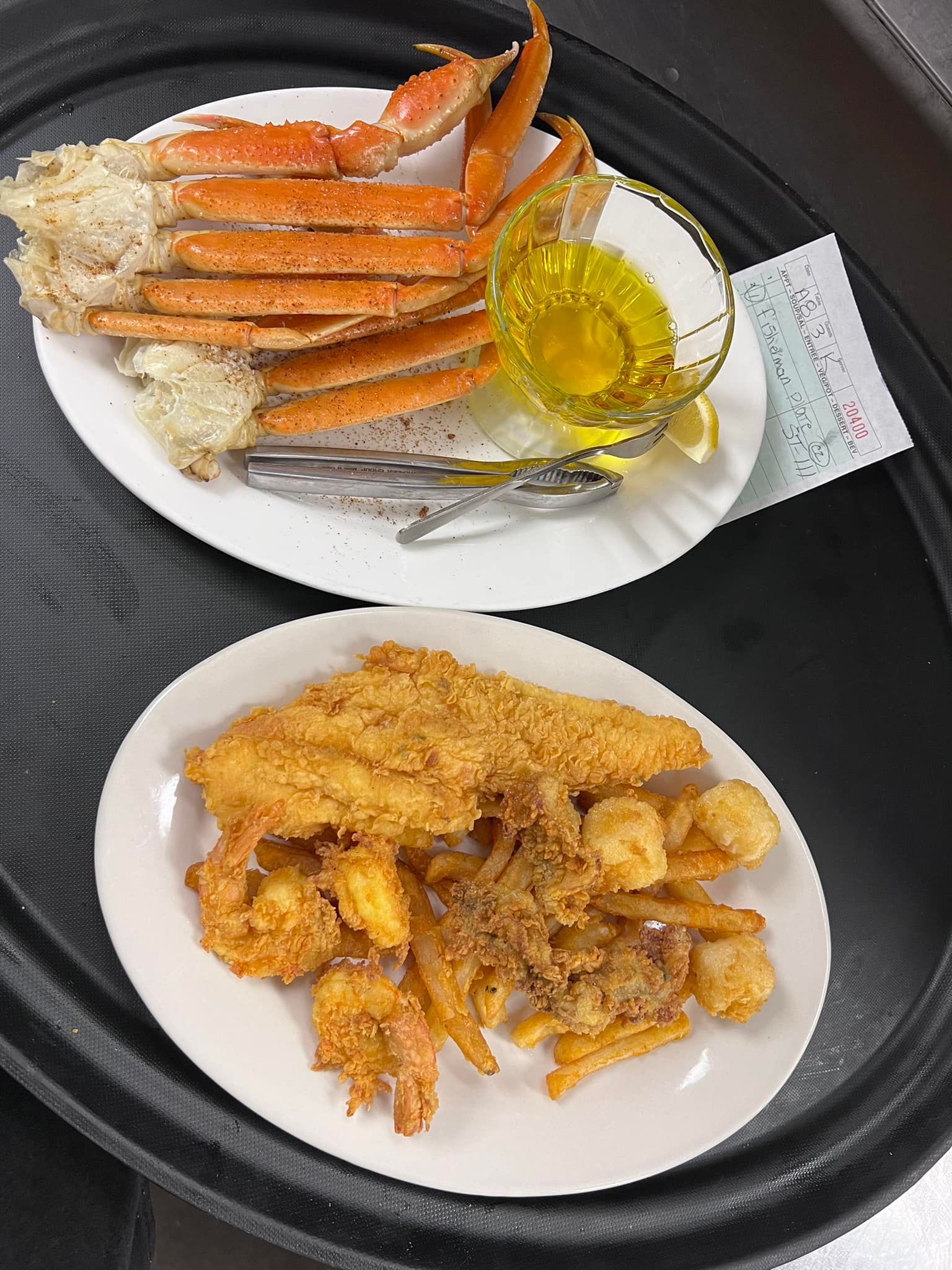 Two plates of fried seafood, rice, and crab legs on a black tray, with a small cup of lemon sauce.