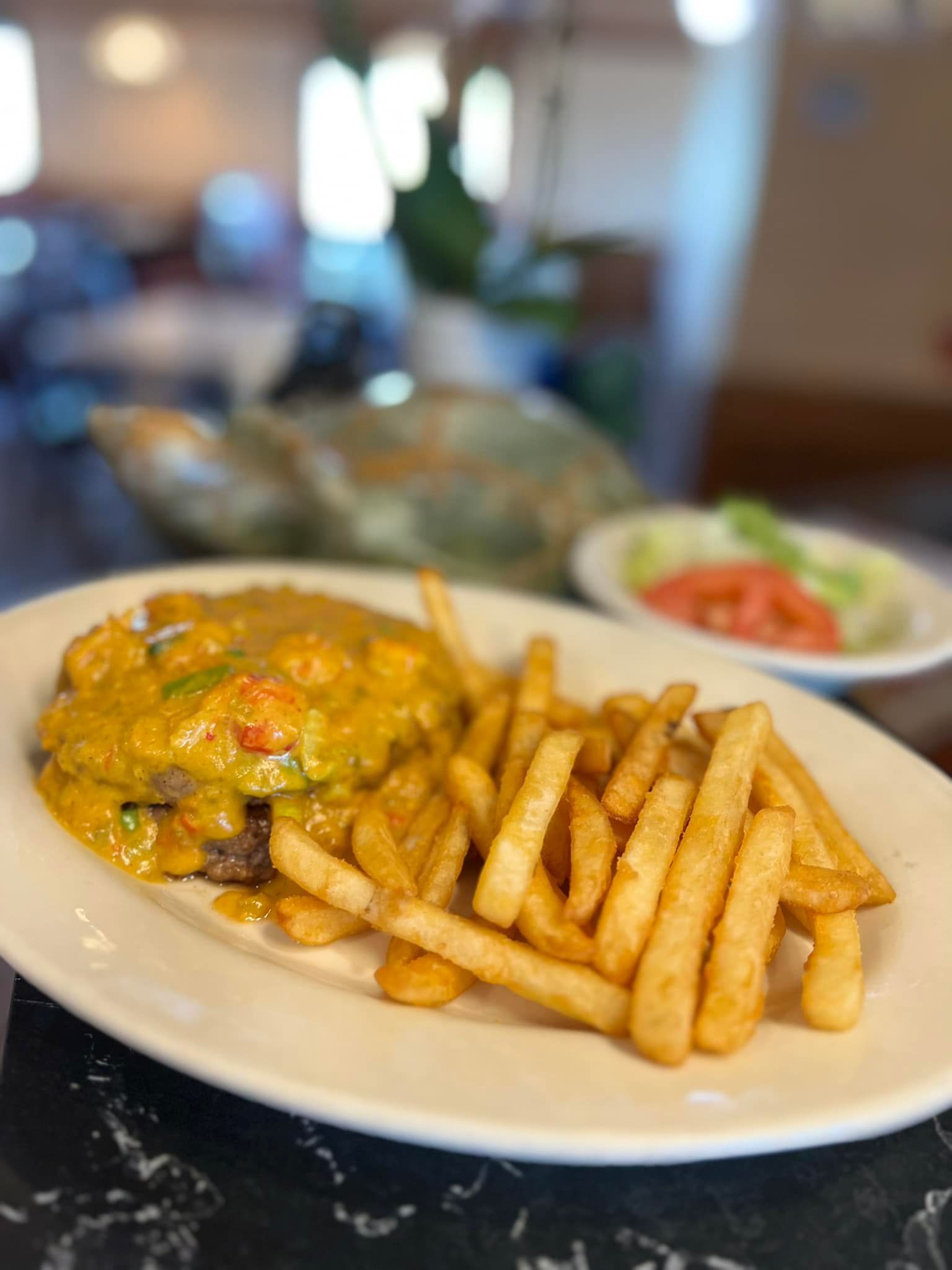 Plate of pasta with fries and a small side salad on a restaurant table, with a blurred dining room in the background