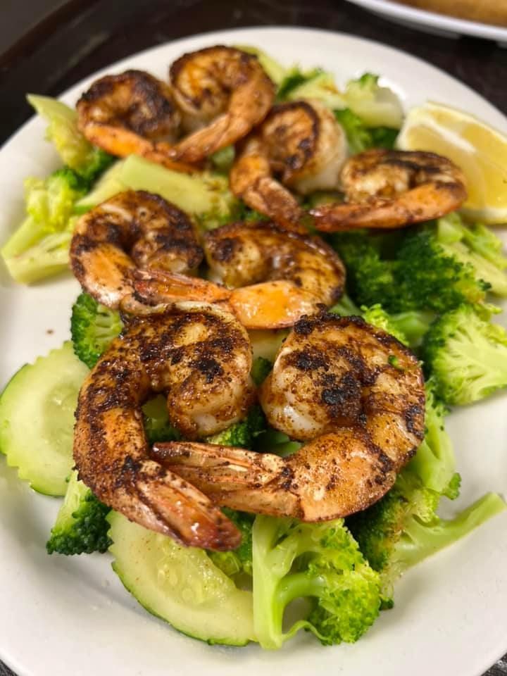 Grilled shrimp atop broccoli and cucumber slices on a white plate