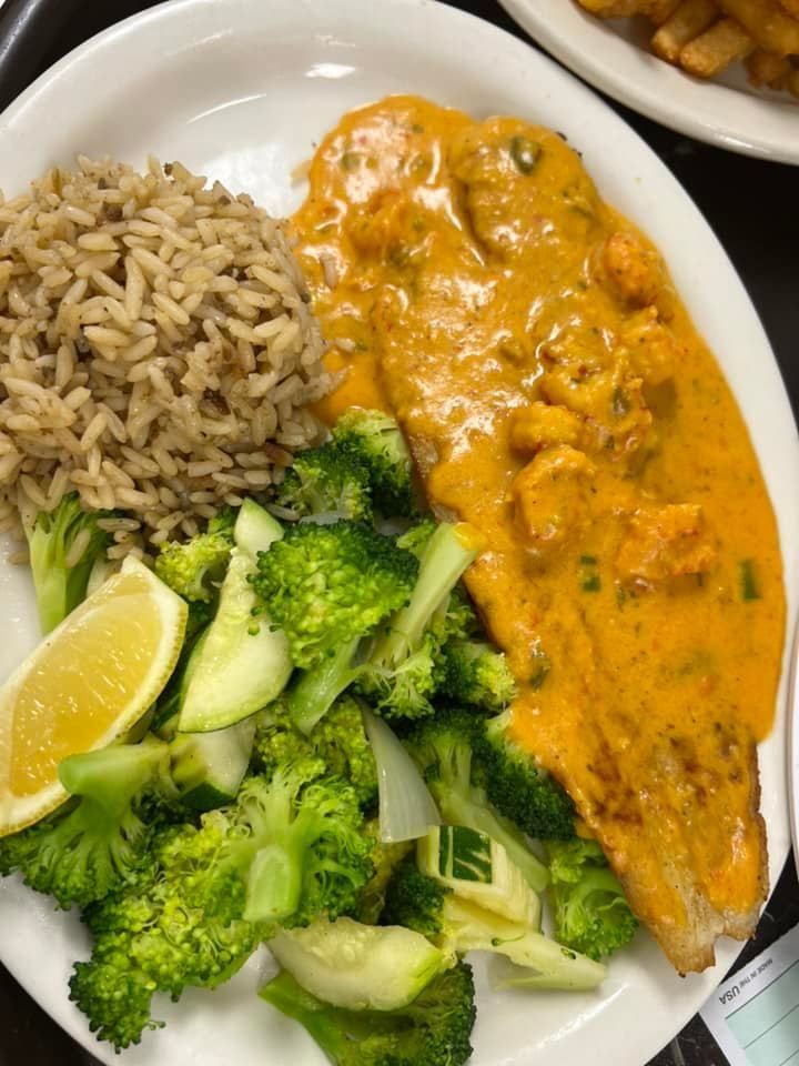 Plate of brown rice, broccoli, and cucumber with a lemon wedge beside orange sauced fish.