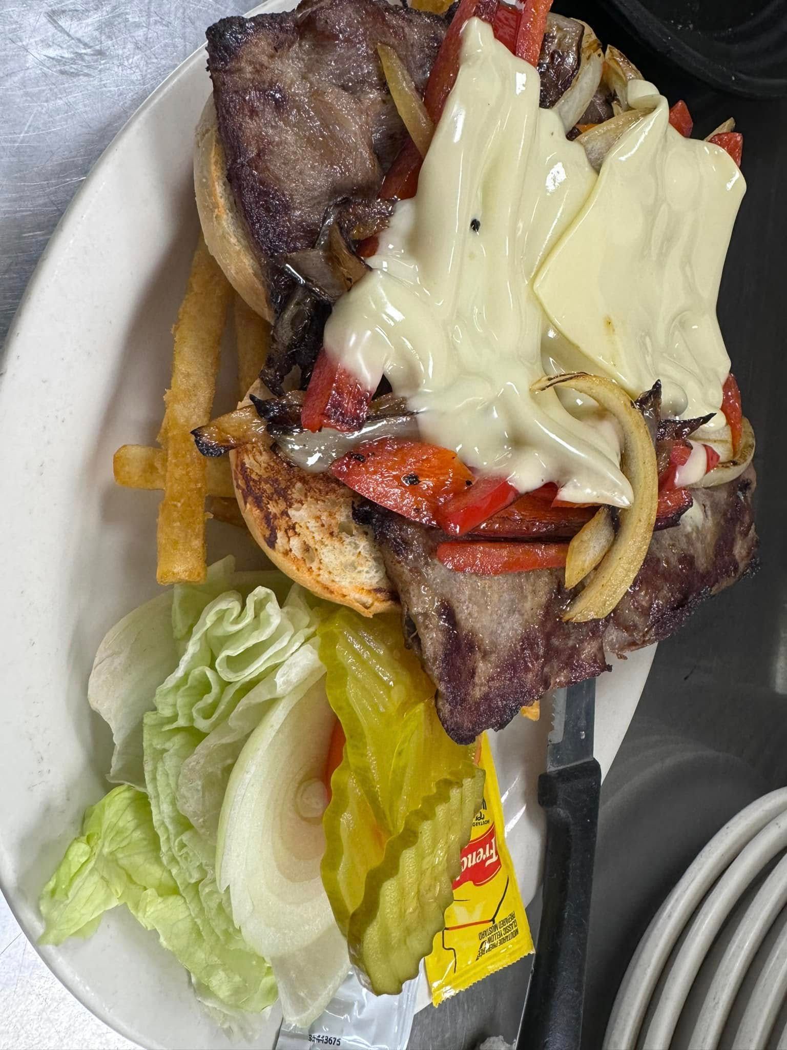 Burger with melted cheese, bacon, lettuce, tomato, and pickles on a plate with fries.