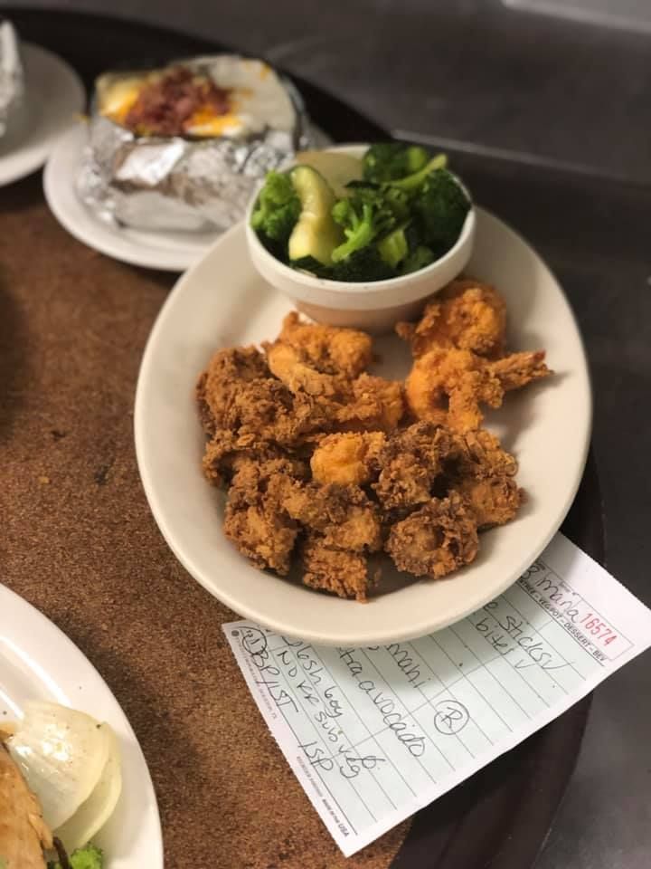 Plate of crispy fried shrimp with broccoli and rice on a restaurant table, with a receipt underneath.