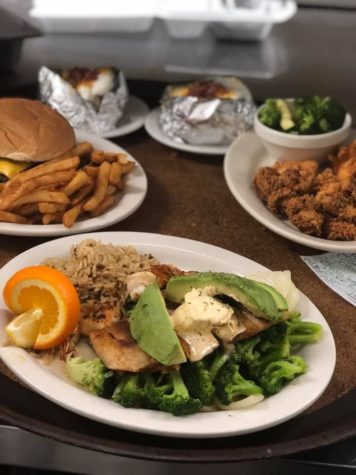 Assorted plates of takeout food, including salad, fries, fried bites, and broccoli, on a table