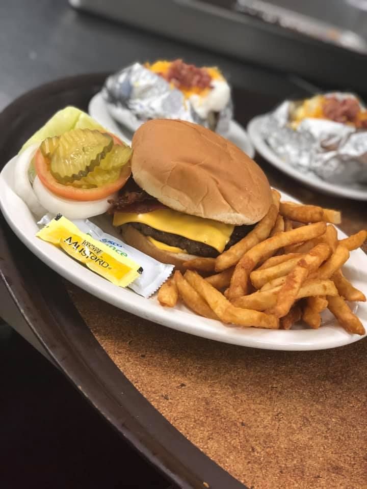Cheeseburger with fries on a plate, plus a wrapped dessert and dipping sauces on a table