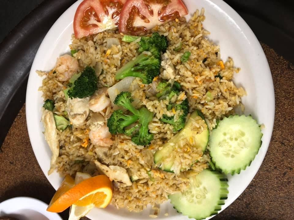 Plate of fried rice with broccoli, cucumber slices, and orange wedges on a white dish