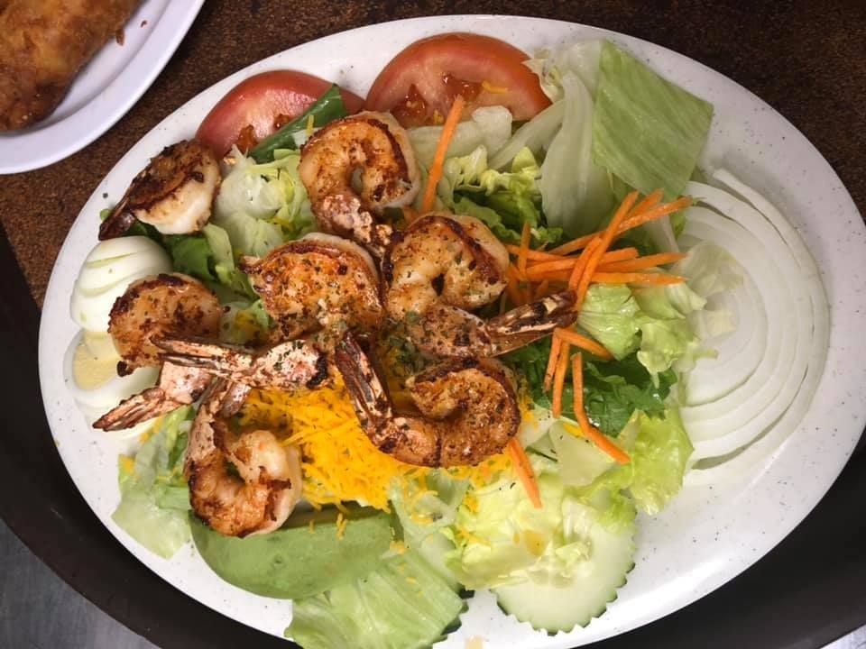 Grilled shrimp salad with lettuce, tomato, carrot strips, cucumber, and onion on a white plate