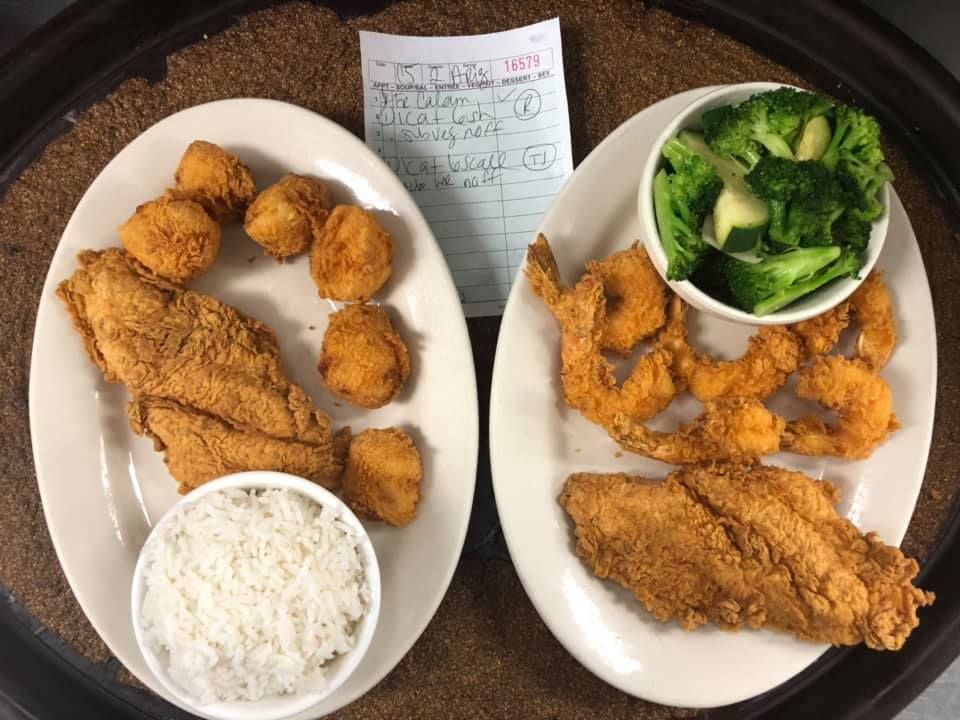 Two plates of fried seafood with rice and broccoli on a table with a receipt.