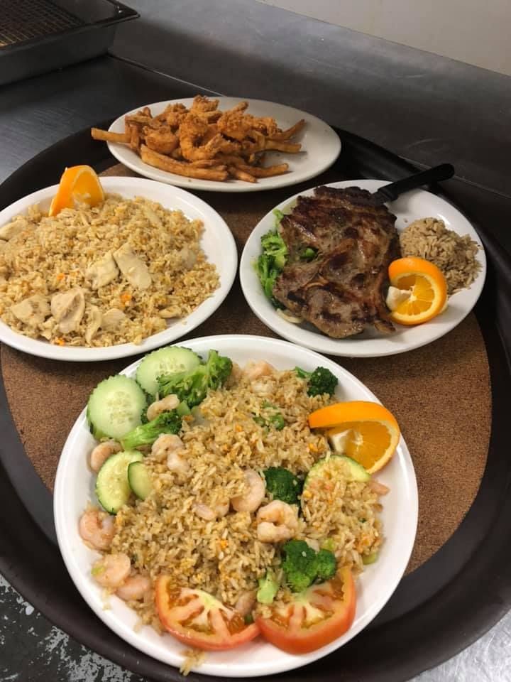 Four plated rice dishes with grilled meats and vegetables on a wooden table