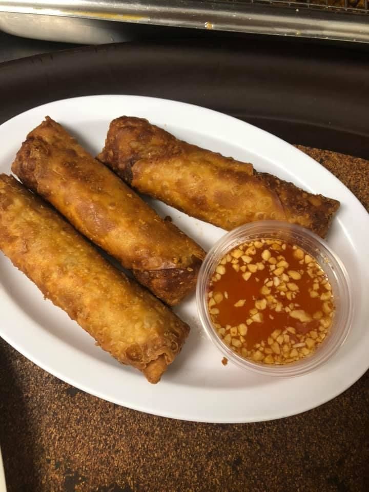 Three fried spring rolls on a white plate with a small cup of dipping sauce