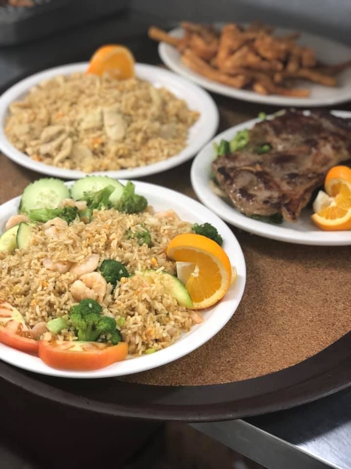 Three plated meals on a table: rice dishes with orange slices, cucumber, and grilled meat.