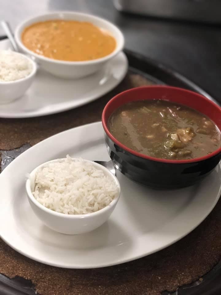Plated meal with rice and soup in white and black bowls on a tray, with an orange sauce dish in the background