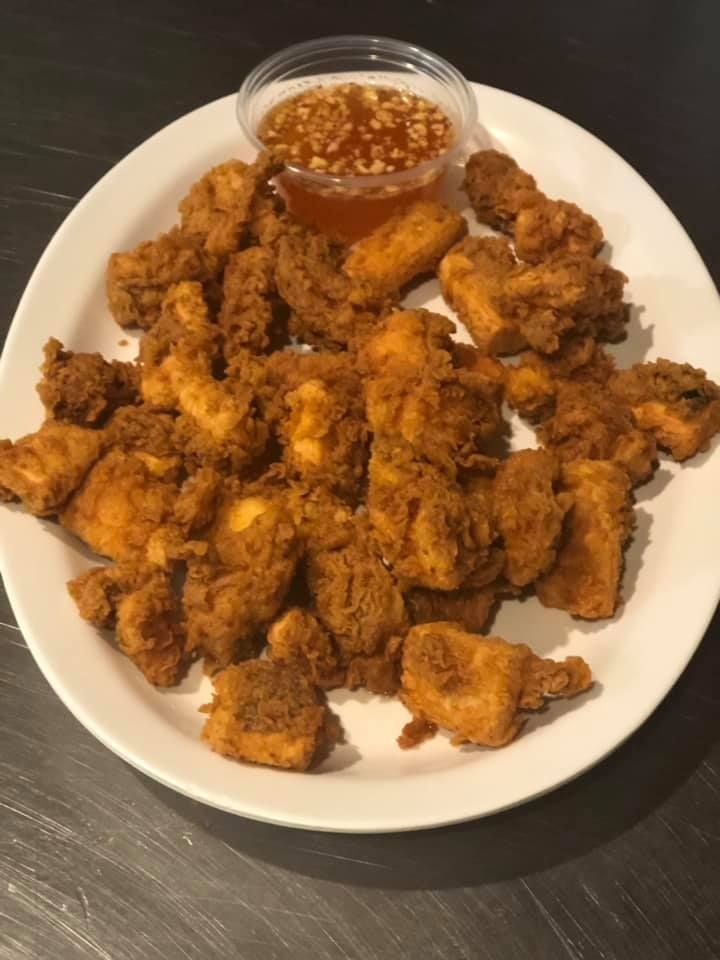 Plate of fried chicken pieces with a small cup of dipping sauce on a dark table