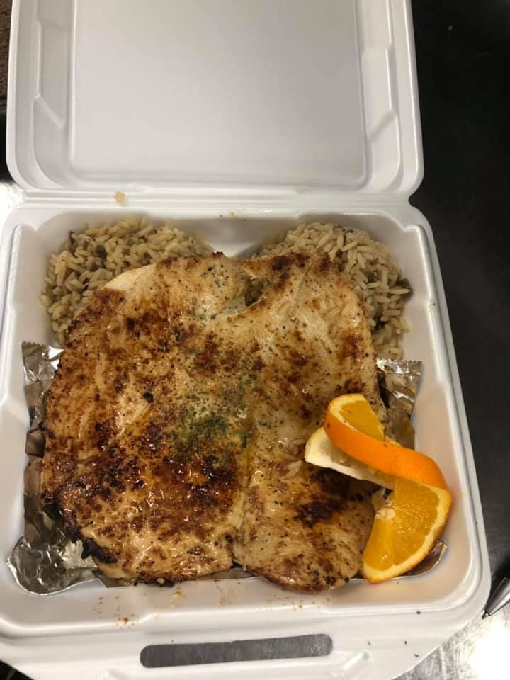 Open foam takeout box with seasoned grilled chicken, rice, and an orange slice.