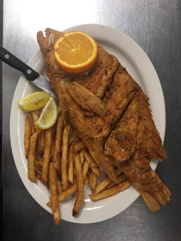 Fried fish and French fries on a white plate with lemon wedges and orange slice
