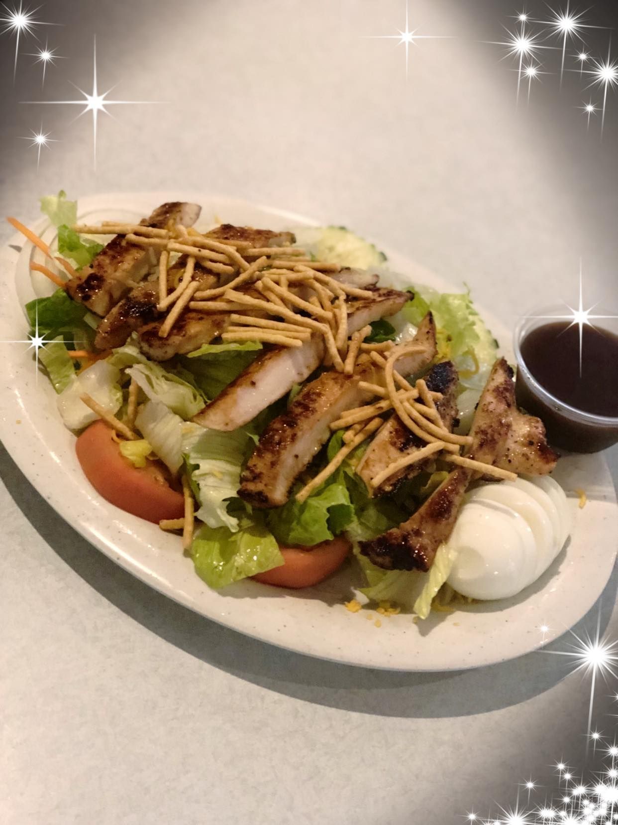 Grilled chicken salad with lettuce, tomatoes, shredded cheese, and crispy strips on a white plate