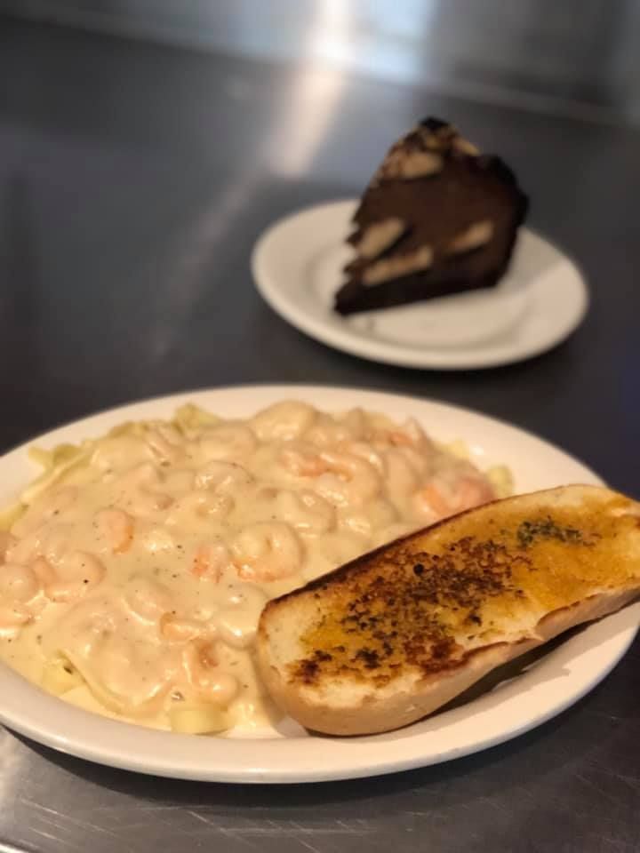 Plate of creamy pasta with toasted bread in the foreground, and a slice of chocolate cake on a plate behind it.