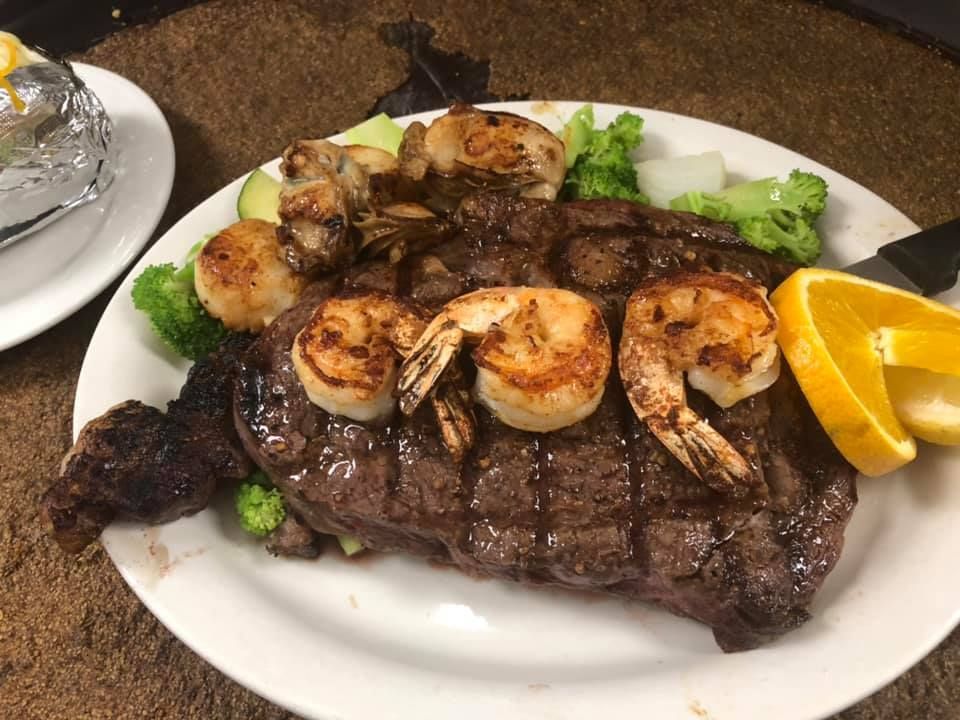 Steak and grilled shrimp on a white plate with broccoli and orange slices on a table