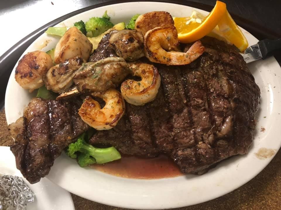 Grilled steak topped with shrimp and orange garnish, served with broccoli on a white plate