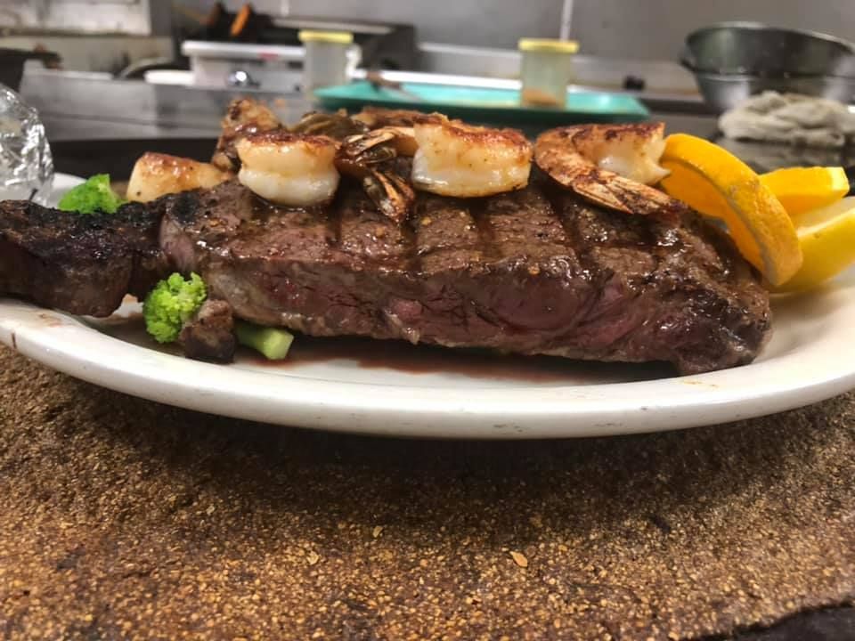 Grilled steak topped with scallops and orange slices on a white plate in a kitchen setting
