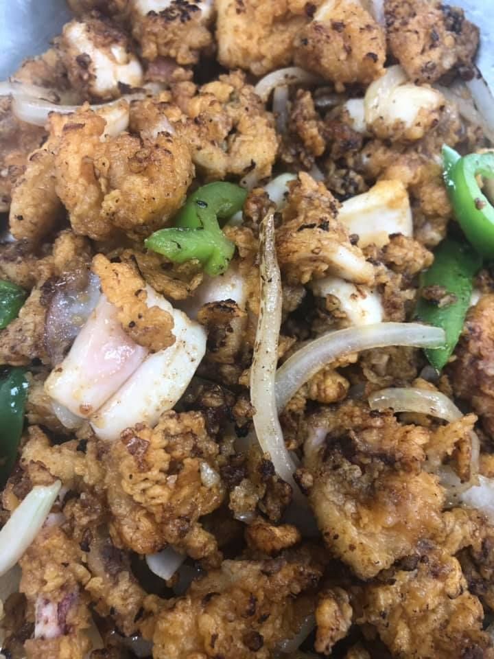 Spicy fried food with onion slices and green chili peppers on a plate
