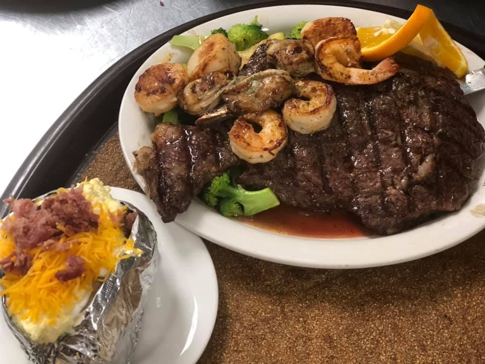 Steak topped with shrimp and mushrooms, plus a baked potato with cheese and bacon on a plate