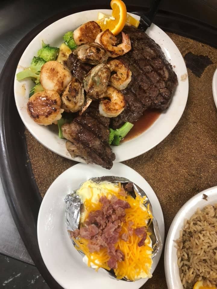 Plated steak with grilled shrimp and orange slices, plus bowls of rice and a cheesy potato side