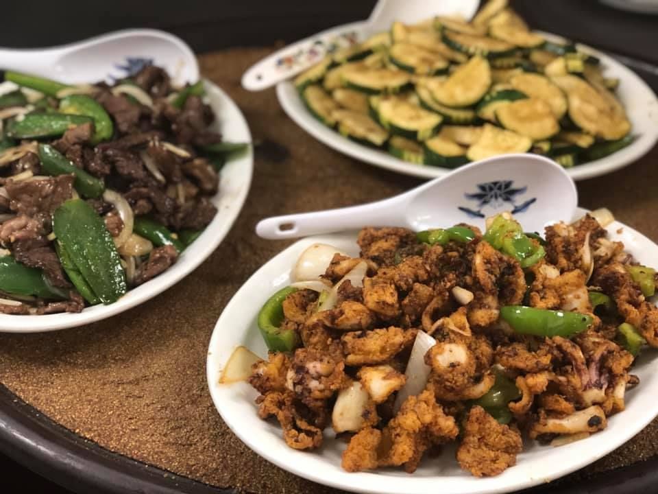Three plates of Chinese stir-fry dishes, including beef, cauliflower, and zucchini, on a table.
