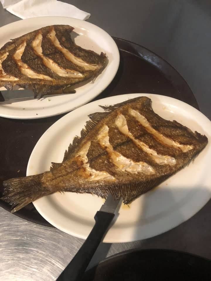 Two whole fried fish on white plates on a metal table