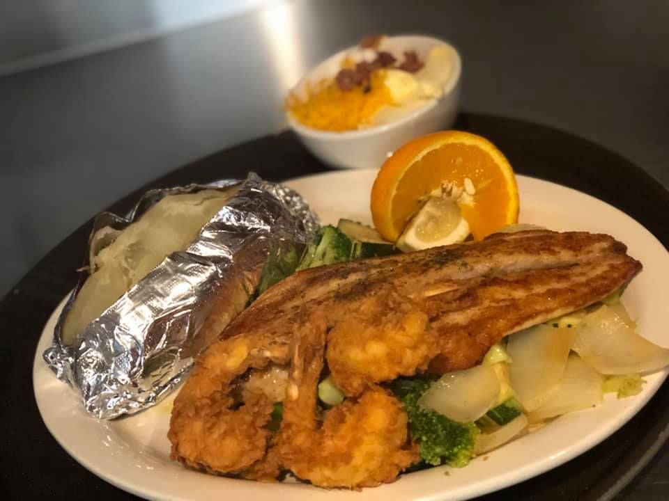 Plated fried fish with baked potato, broccoli, and orange slices, with a dessert cup in the background