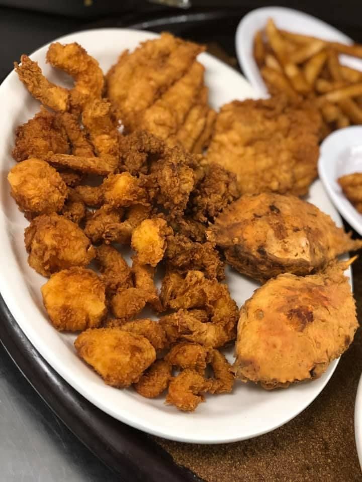 Plate of fried seafood and hush puppies with fries on a table