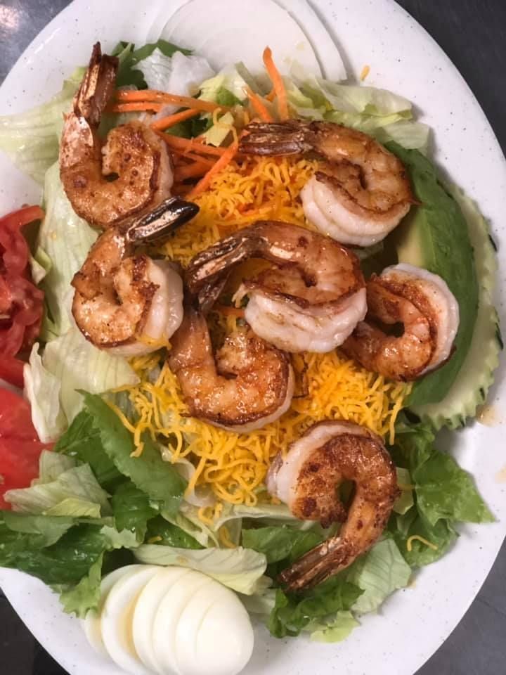 Shrimp salad with lettuce, shredded cheese, carrots, and sliced boiled eggs on a white plate