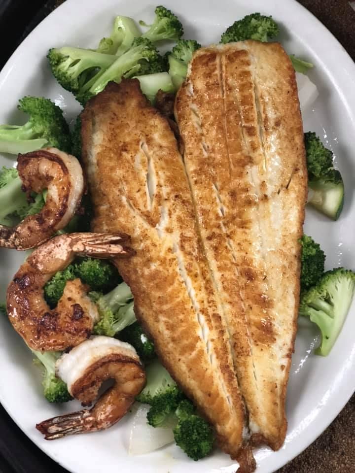 Grilled fish fillet with shrimp and broccoli on a white plate