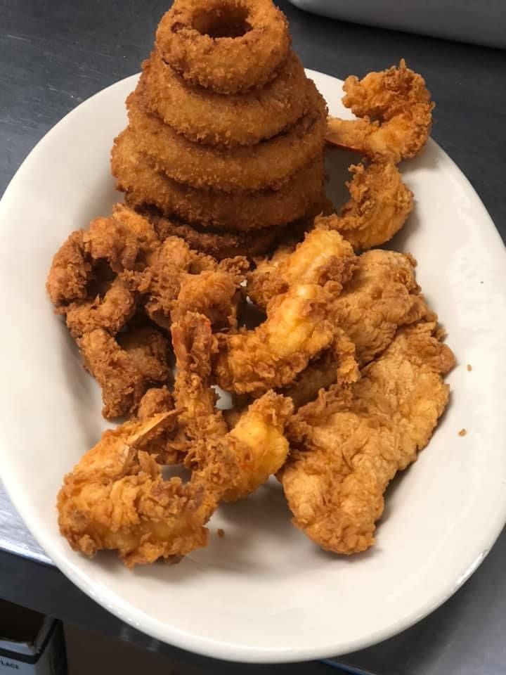 White plate with fried chicken pieces and stacked onion rings on a plain surface