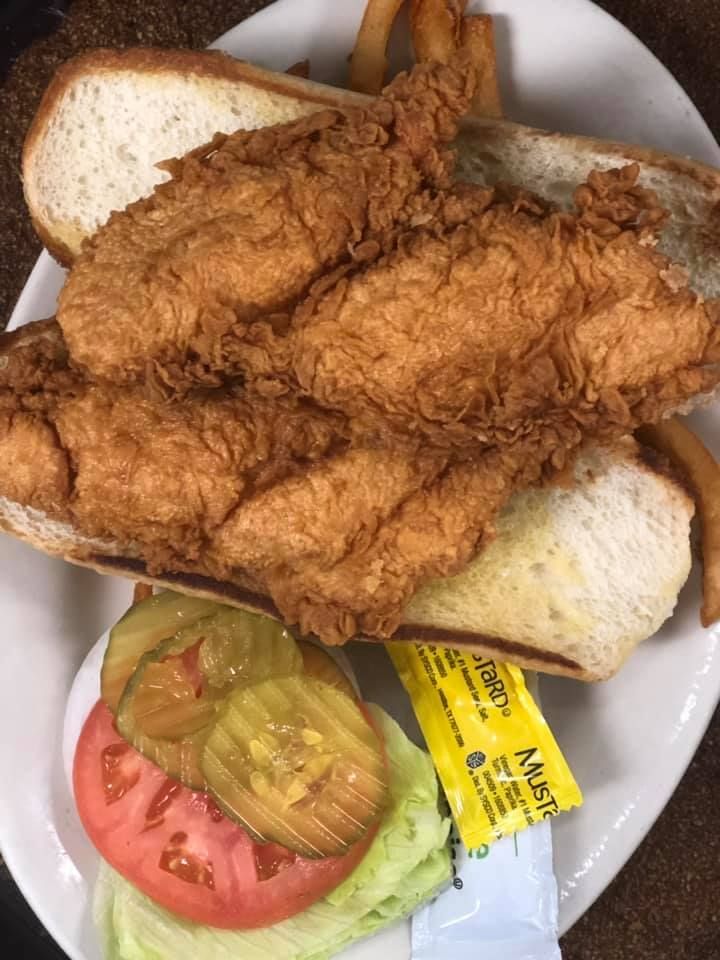 Fried fish sandwich on a white plate with lettuce, tomato, pickles, and bread slices