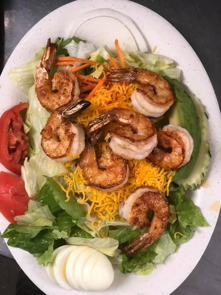 Shrimp salad with lettuce, shredded cheese, tomato, cucumber, and hard-boiled eggs on a white plate