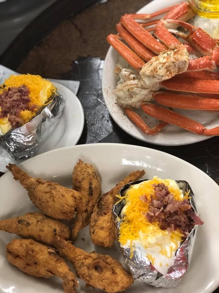 Seafood meal with crab legs, fried chicken, and loaded baked potatoes on white plates