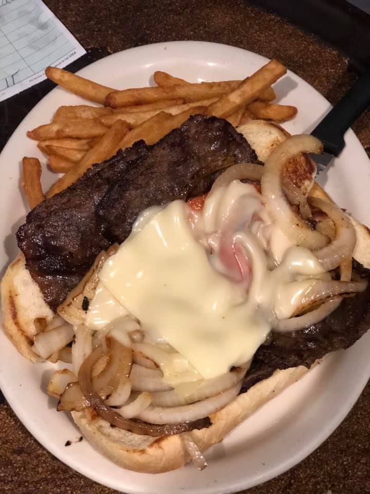 Cheesesteak sandwich with melted cheese and onions, served with fries in a white bowl