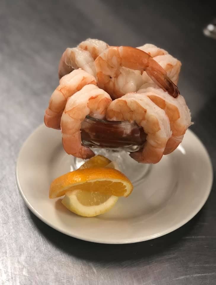 Shrimp arranged in a glass on a saucer with a lemon wedge on a stainless-steel counter