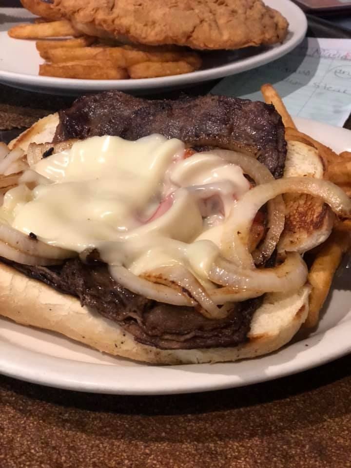 Cheeseburger with melted cheese and onions on a plate, with fries in the background