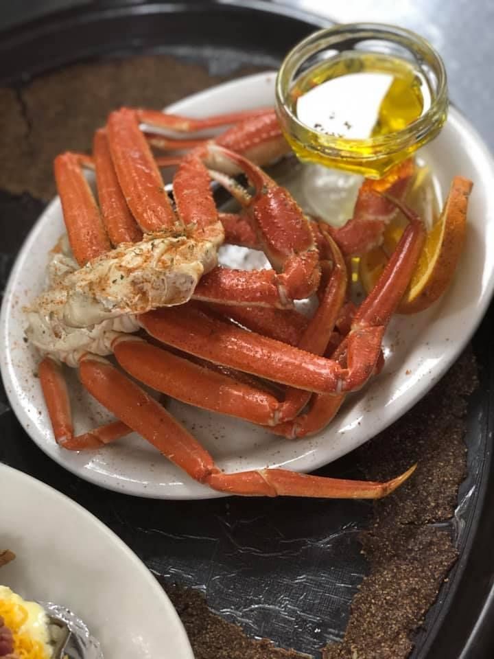 Crab legs on a white plate with melted butter in a glass cup on a dark table