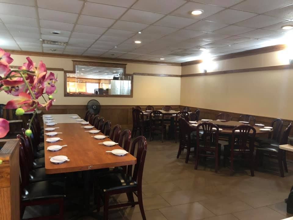 Empty restaurant dining area with long wooden tables, dark chairs, and pink flowers in the foreground