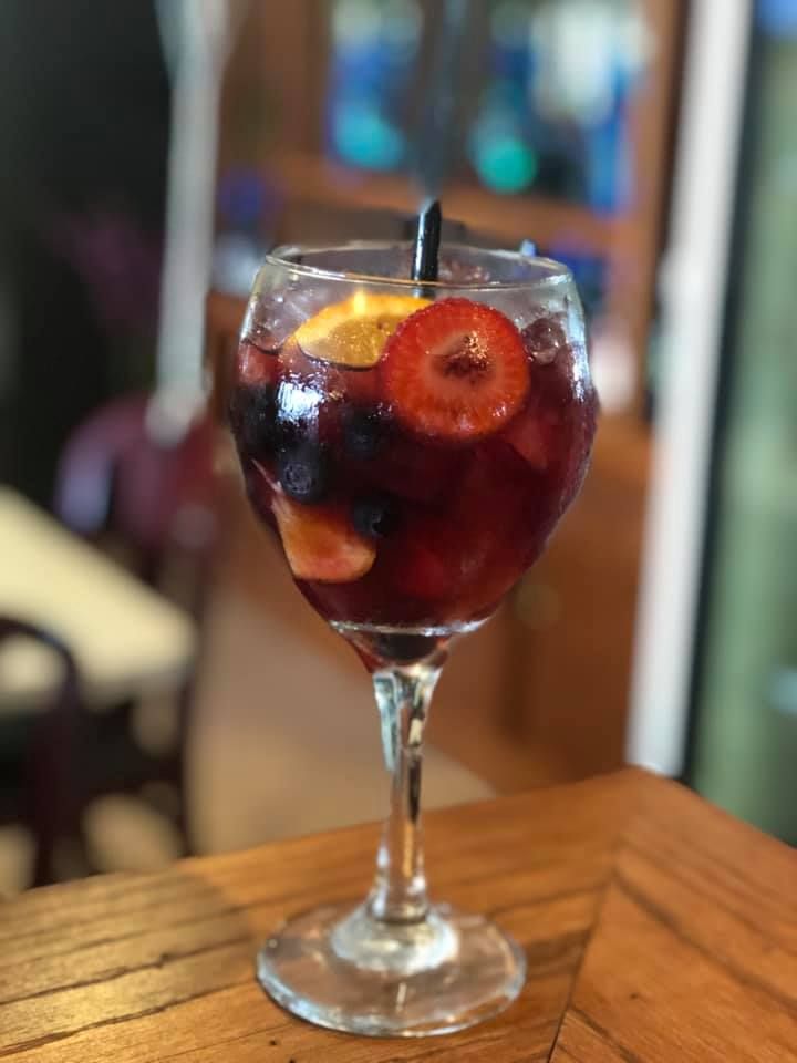 Stemmed glass of red sangria with fruit slices on a wooden table in a blurred café setting